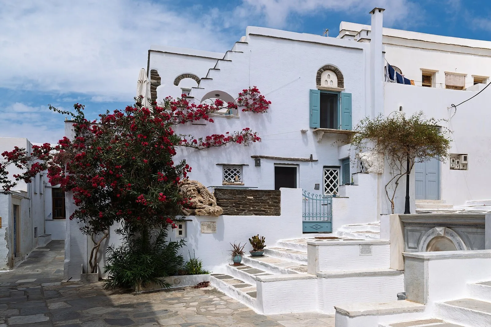 Κόκκινη βουκαμβίλια μπροστά από λευκό κυκλαδίτικο σπίτι με γαλάζια πόρτα στην Τήνο